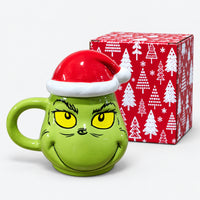 Green character mug with Santa hat lid next to its red Christmas tree gift box