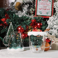 Christmas tree glass mugs with snow lids next to a Christmas tree