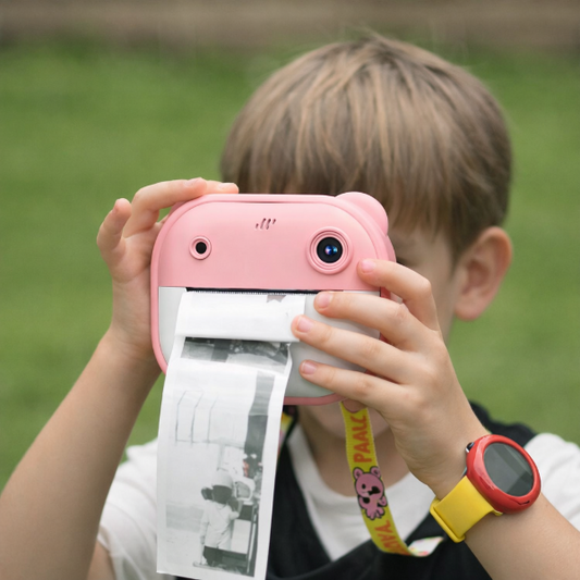 Child holding a pink instant camera with a printed photo, outdoors.