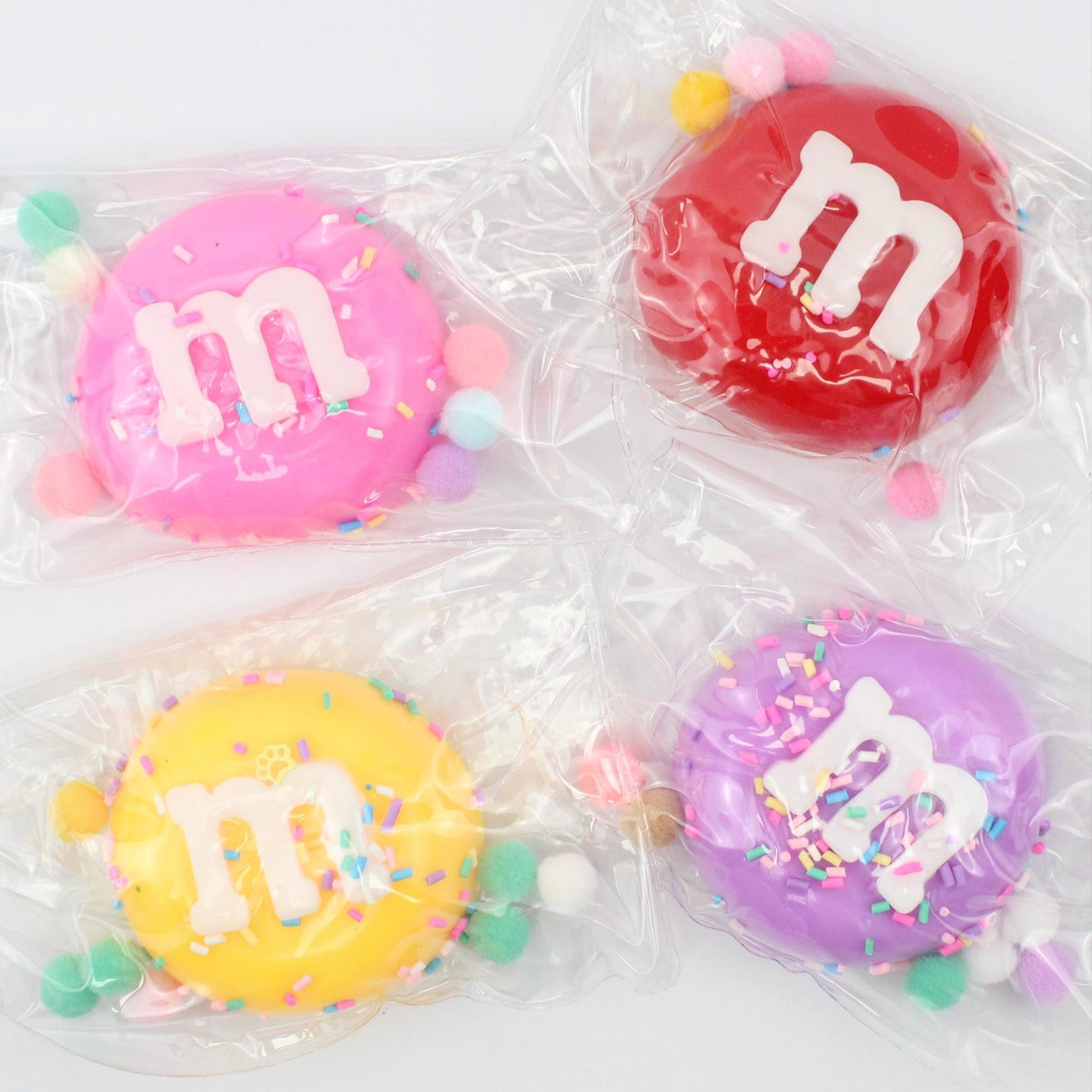 Four colorful M&M candies in clear packaging on a white background