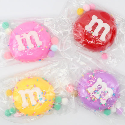 Four colorful M&M candies in clear packaging on a white background