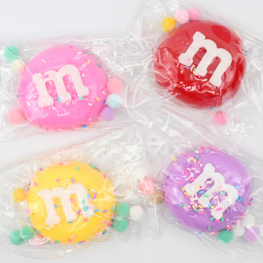 Four colorful M&M candies in clear packaging on a white background