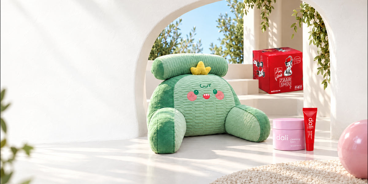 A sunlit white arch opening onto a garden, staged with Afkar Plus finds: a plush back-support pillow, the 7zar Shou game, Dali cleansing balm and lip butter