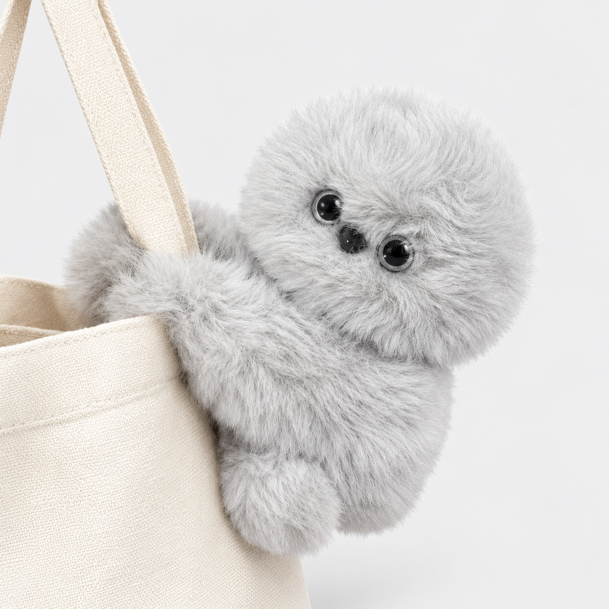 Light gray plush bag charm hugging a bag strap