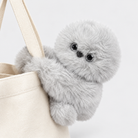 Light gray plush bag charm hugging a bag strap